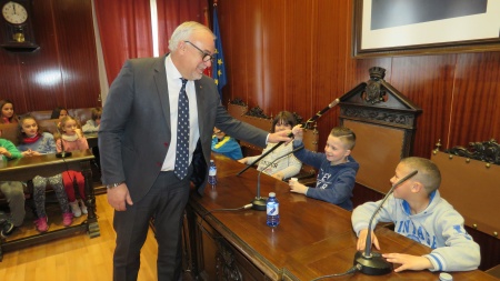 El alcalde entrega su bastón de mando al alumno que ocupa su lugar en el salón de plenos